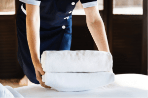 Maid folding white sheets on bed