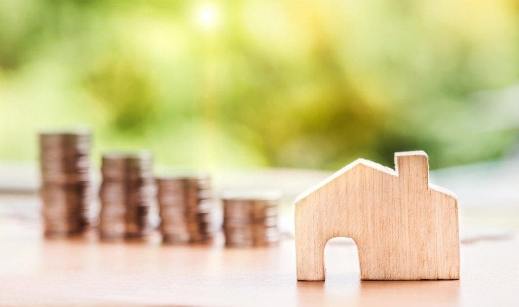 A model wooden house in front of piled up coins