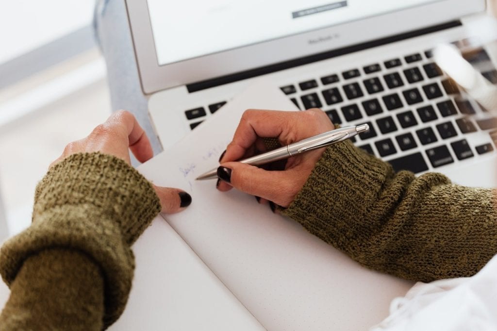 A woman writing next to a laptop